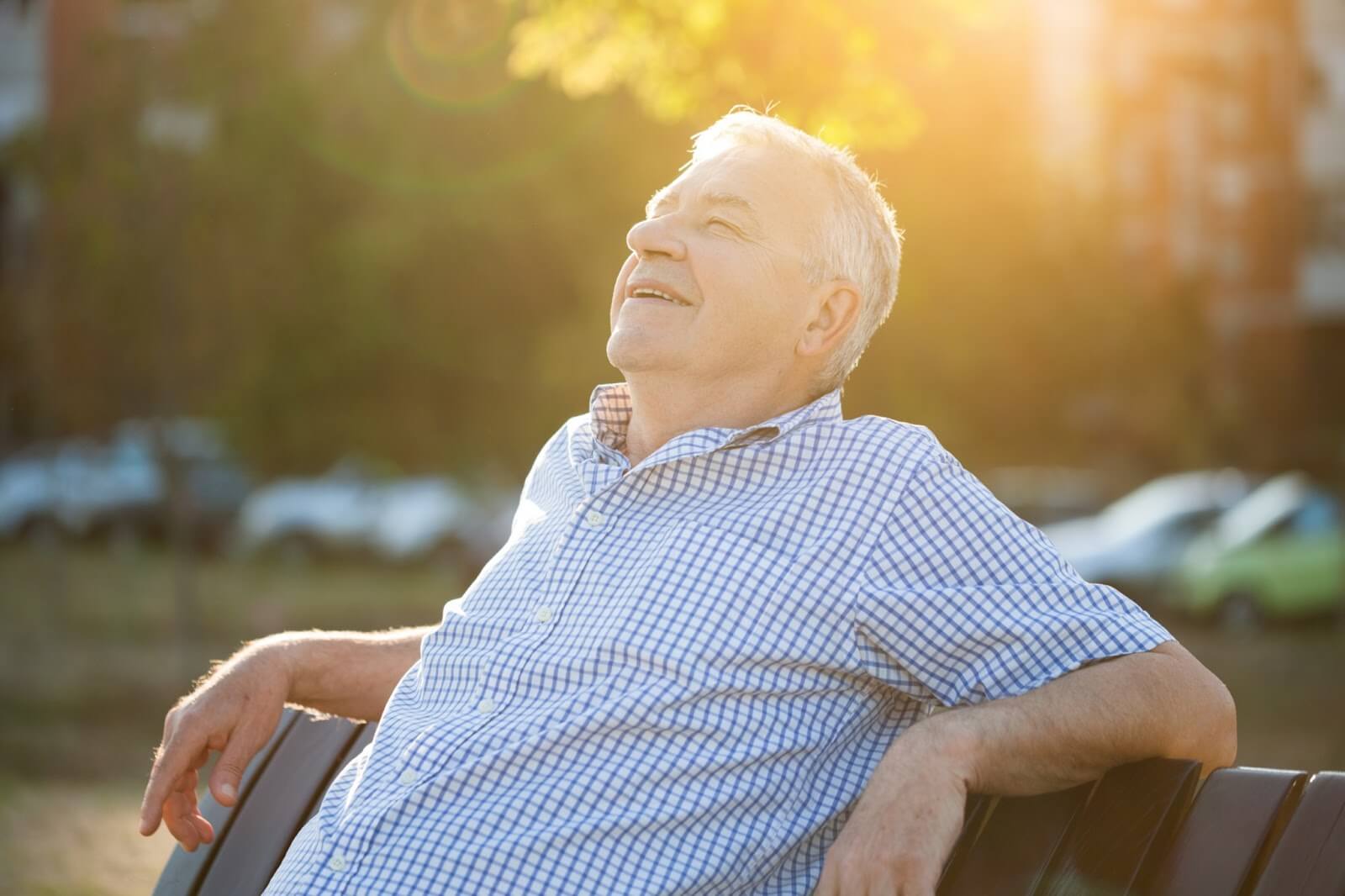 A mature man relaxing on a bench in the sunshine with a smile on his face.