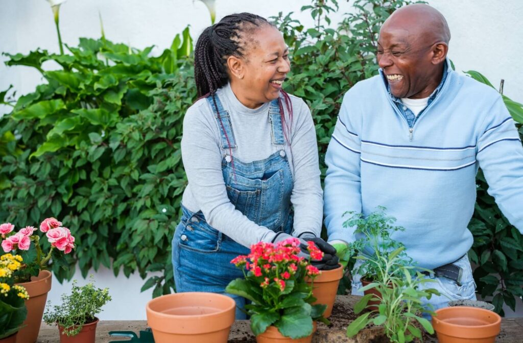 Two older adults smiling and gardening together, enjoying a shared outdoor activity in an assisted living community.