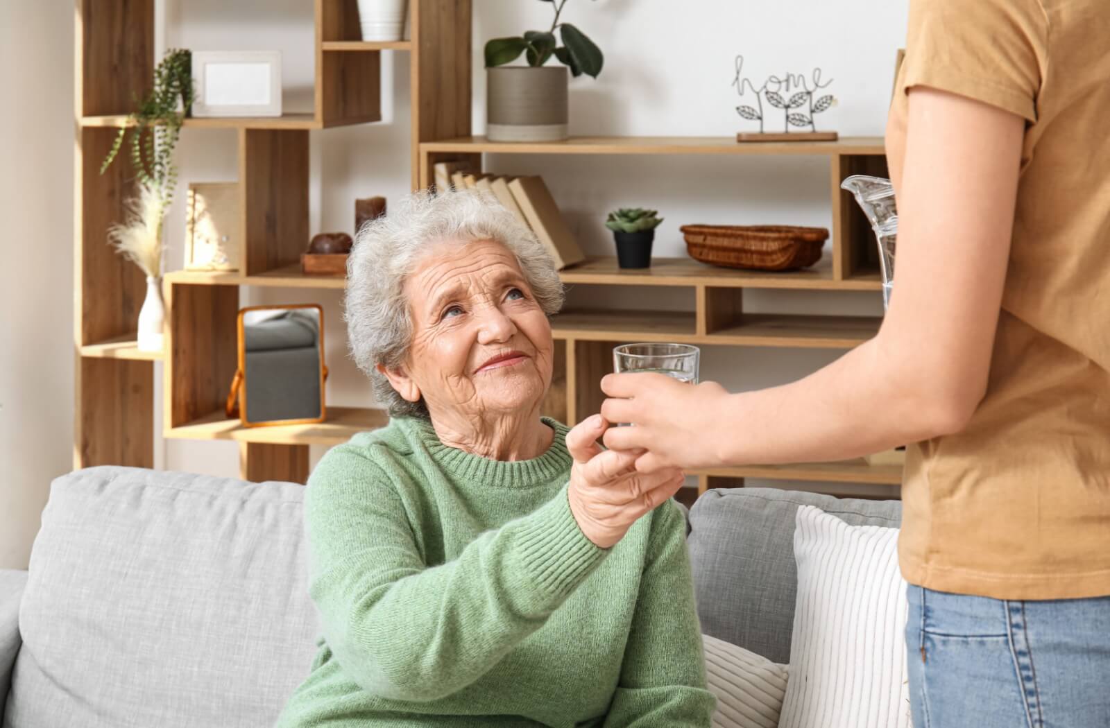 Caregiver offering a glass of water to an older adult woman with Alzheimer’s.