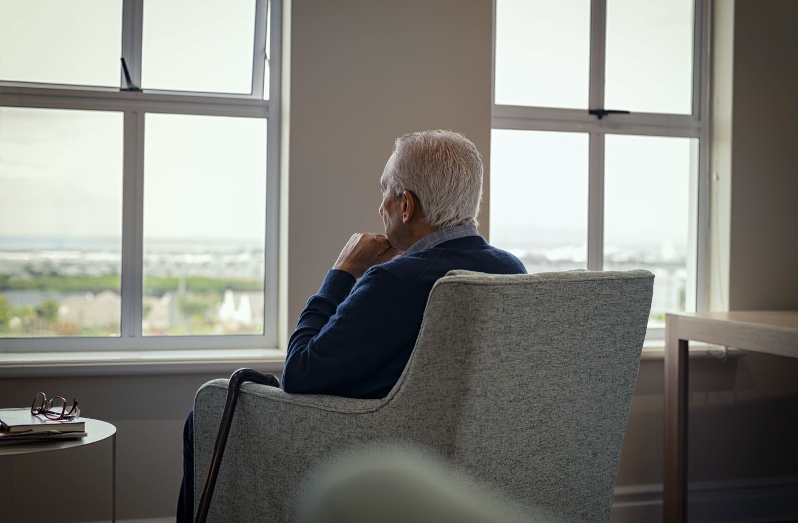 A grieving older adult stares out a window in their home.