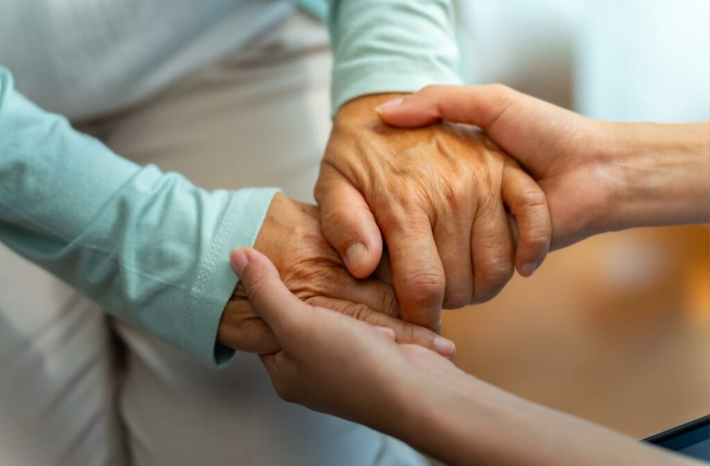 A close-up of a caregiver and an older adult holding hands in consolment.