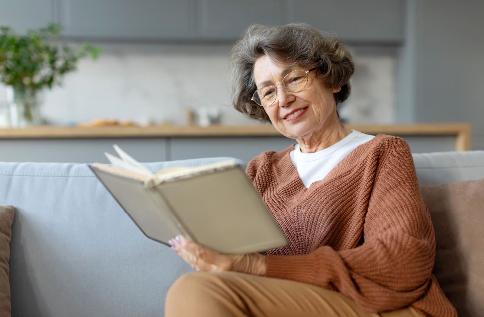 An older adult reads a book while lounging comfortably on the couch.