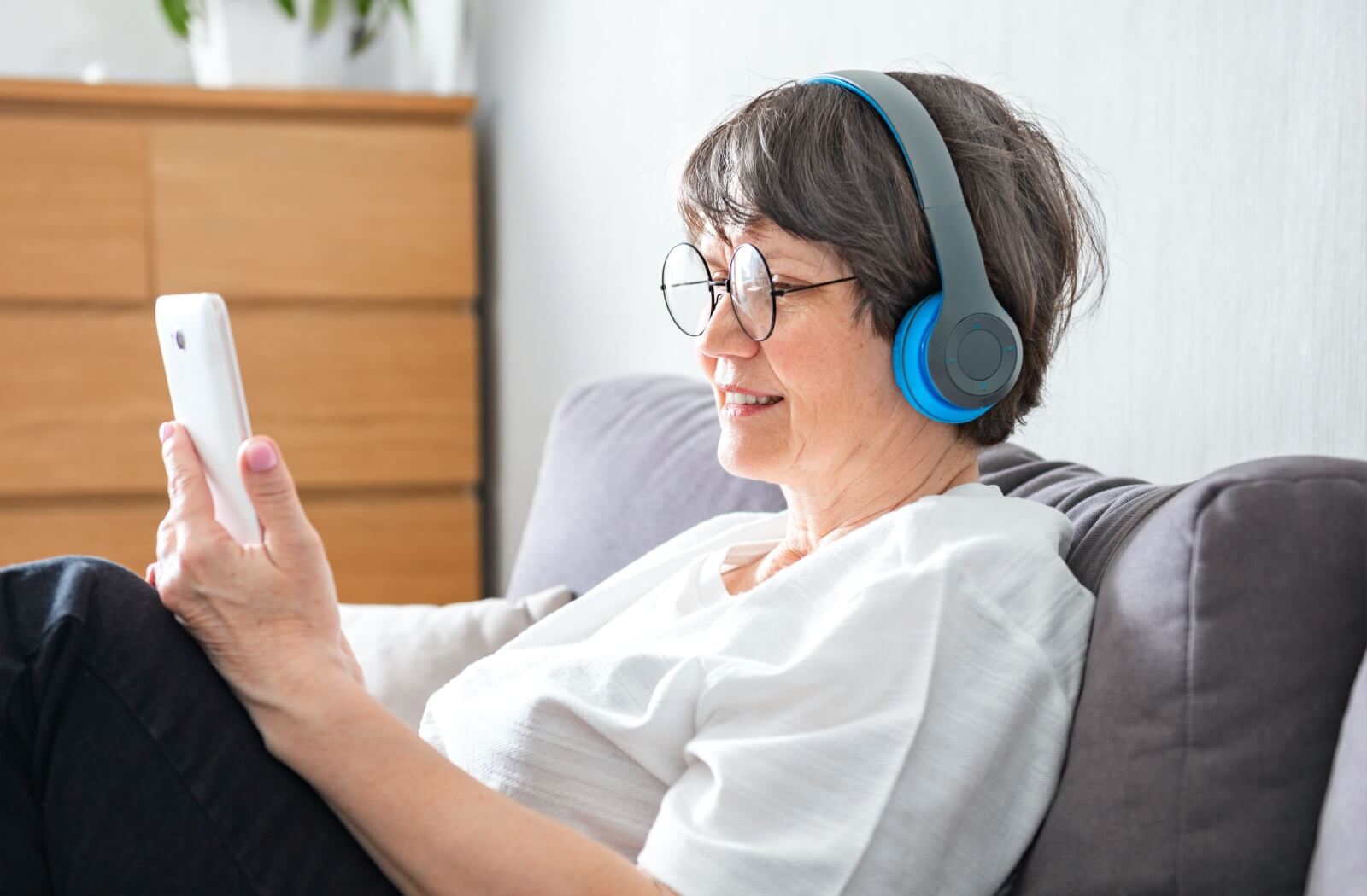 An older adult smiling while looking at their phone and listening to an audiobook through headphones.