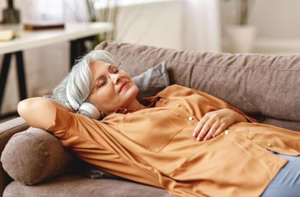 An older adult lying on the couch and listening to a new audiobook with their eyes closed.