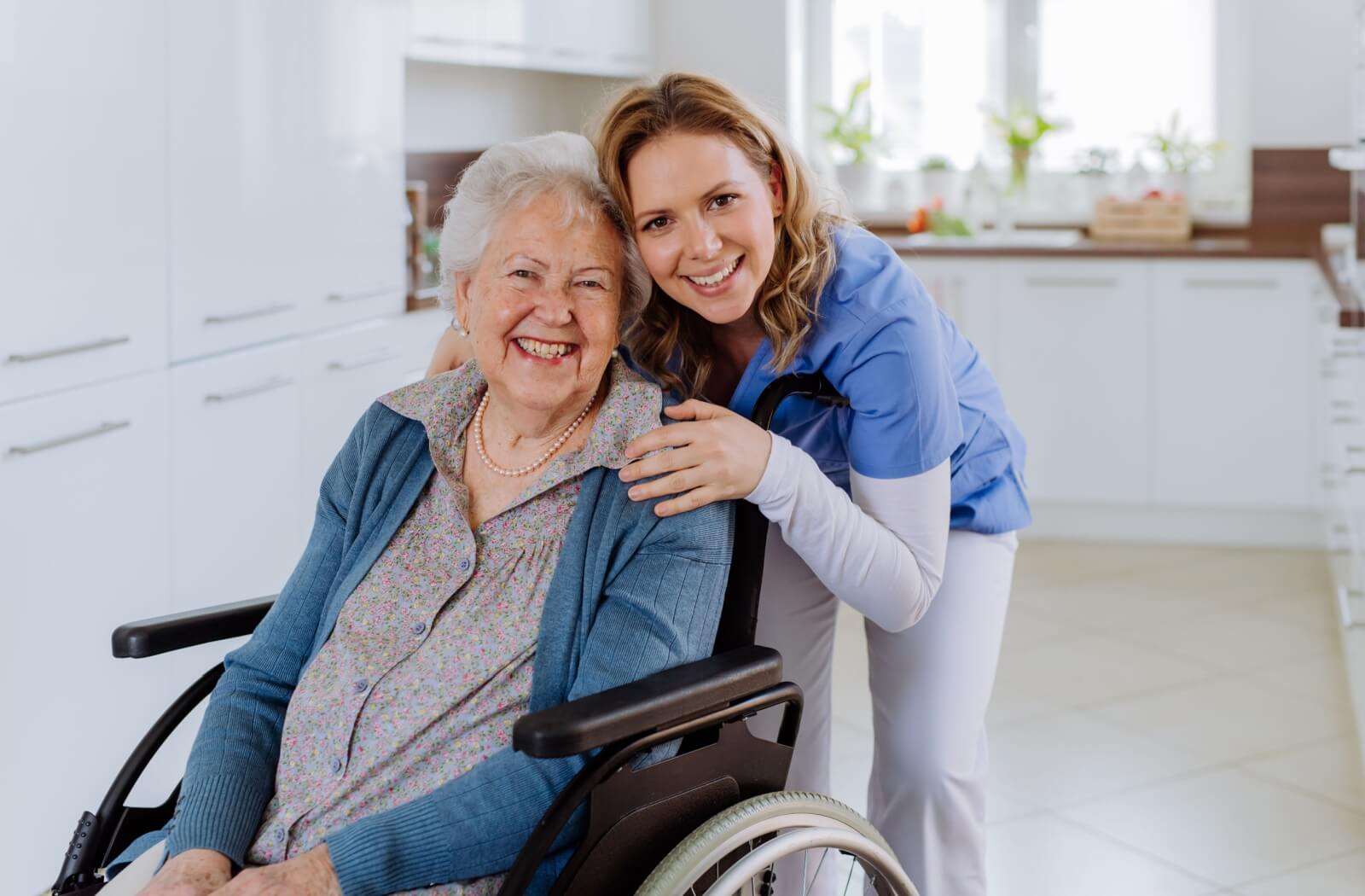 A caregiver hugging an older adult in a wheelchair from behind in the kitchen of a personal care home.