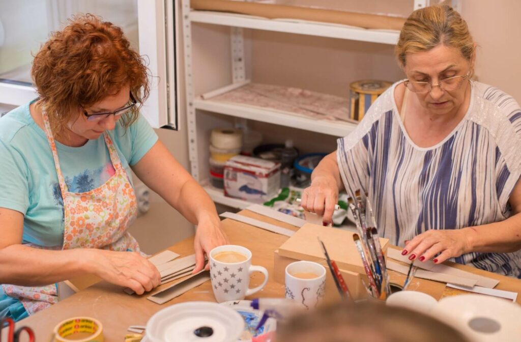 Two older adults working with cardboard strips making a memory box together in memory care