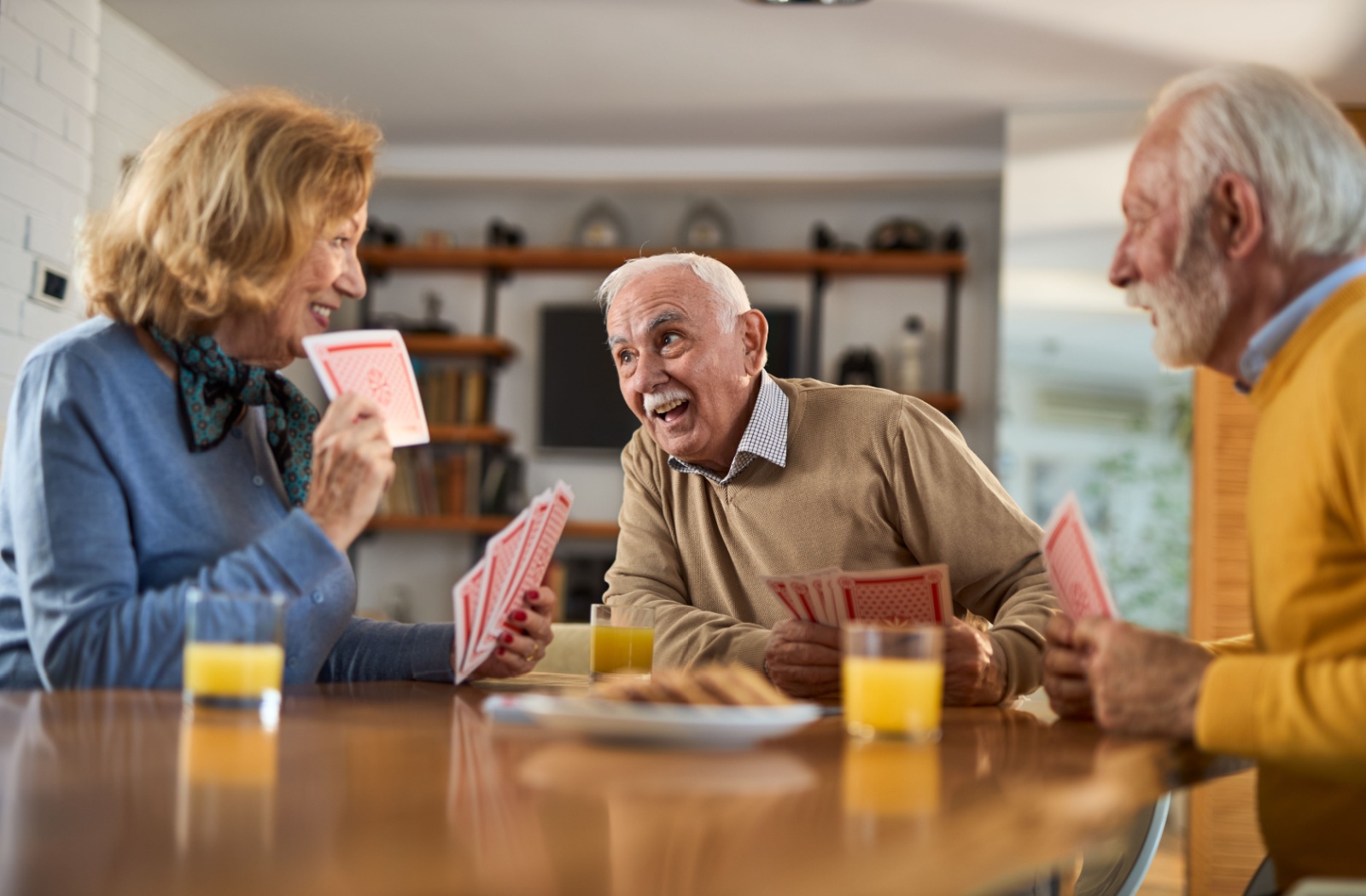 A group of older adults laughing and playing cards together in an assisted living community.