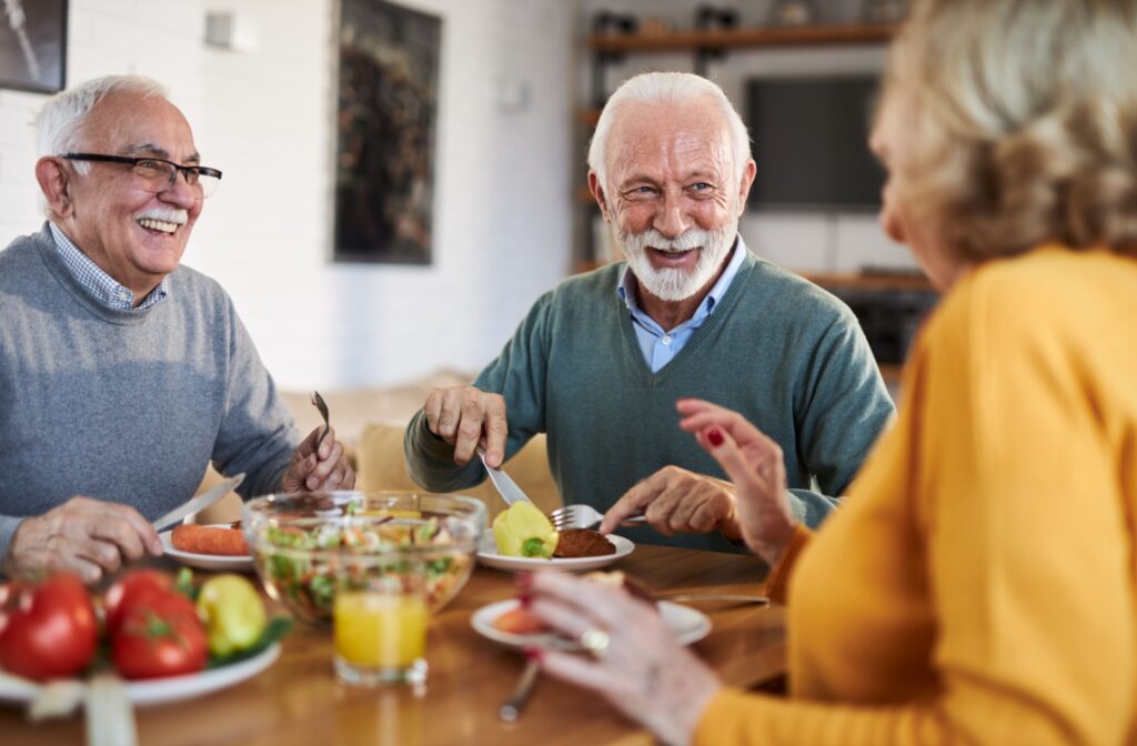 A group of smiling older adults sharing a meal together in assisted living.