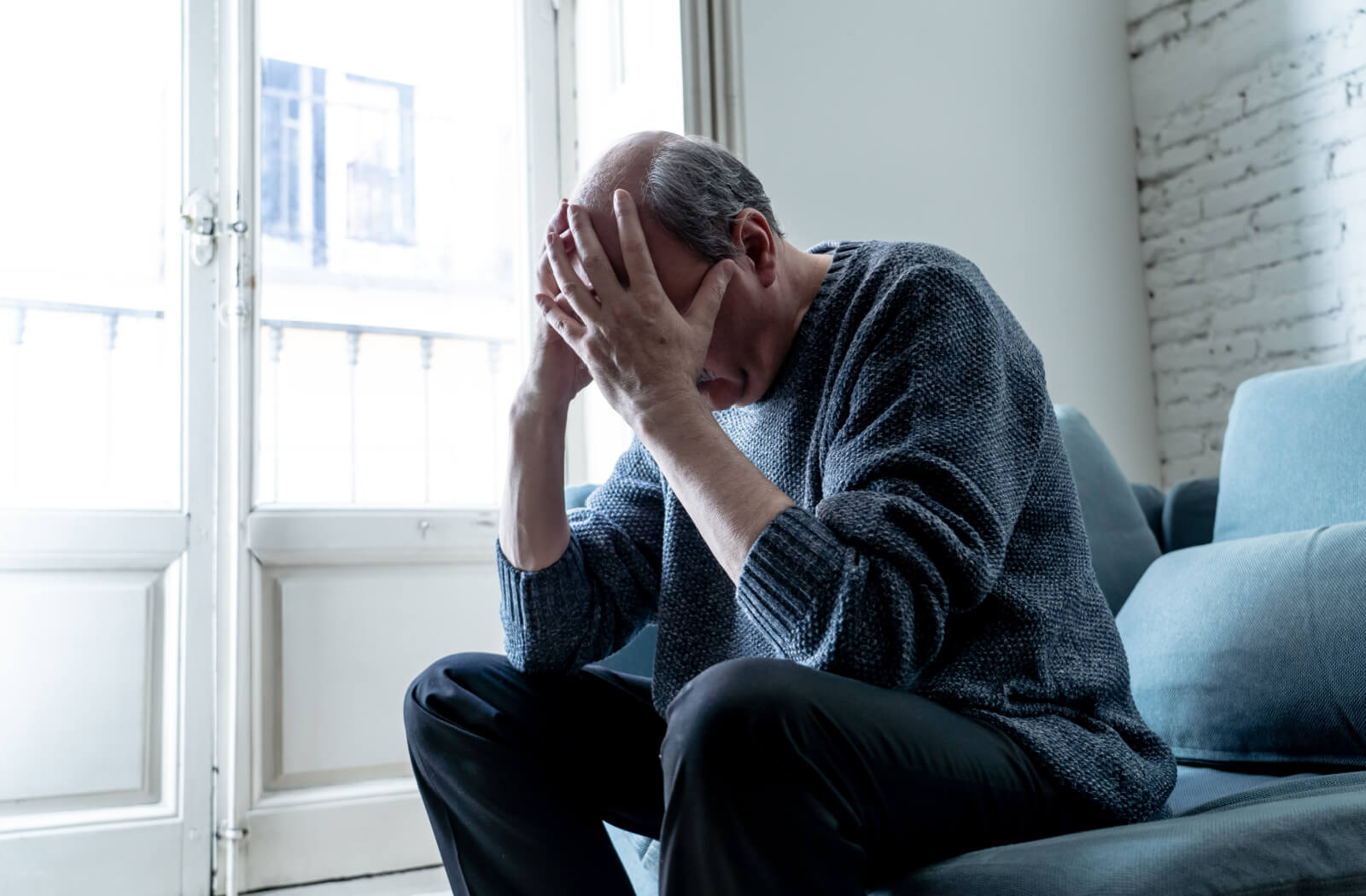 A senior man sitting on a couch in his living room showing signs of depression and loneliness.