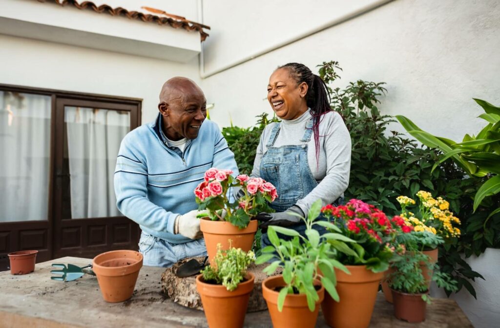 Two older adults laugh while potting flowers outdoors together as a group activity that compensates for their mobility issues