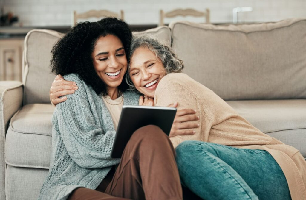 An older adult laughing and hugging their adult child during a visit to their memory care home